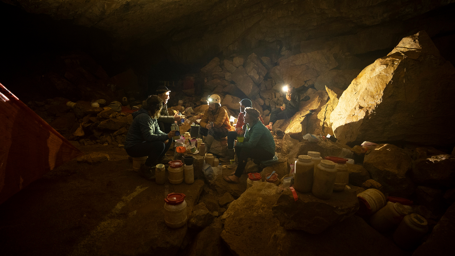 Team members eat a meal at one of the Cheve Cave camps surrounded by their gear and food packs.... [Photo of the day - June 2022]