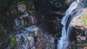 Hazen Audel standing on a cliff beside a waterfall. This is from Primal Survivor: Ultimate Journey. Photo of the day -  9 August 2022