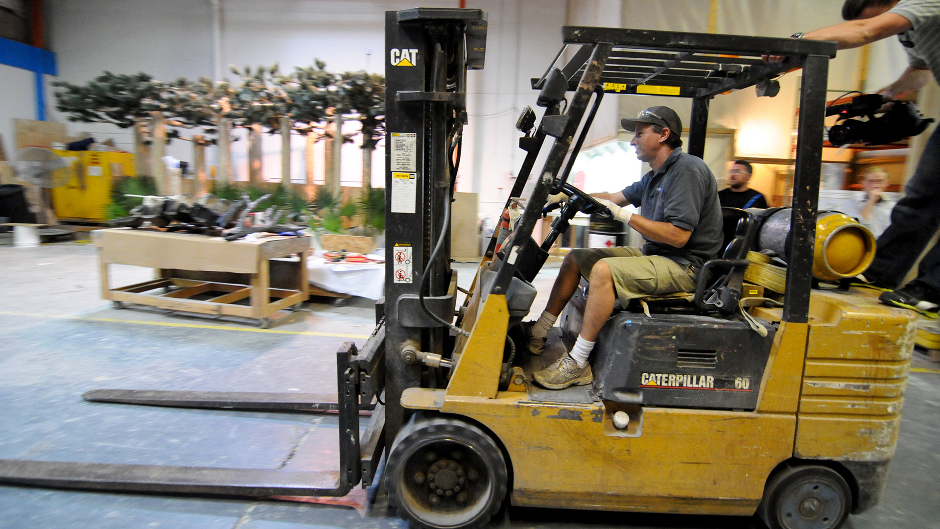Jose driving forklift in warehouse with crew member filming. This is from Fish Tank Kings. [Photo of the day - April 2023]
