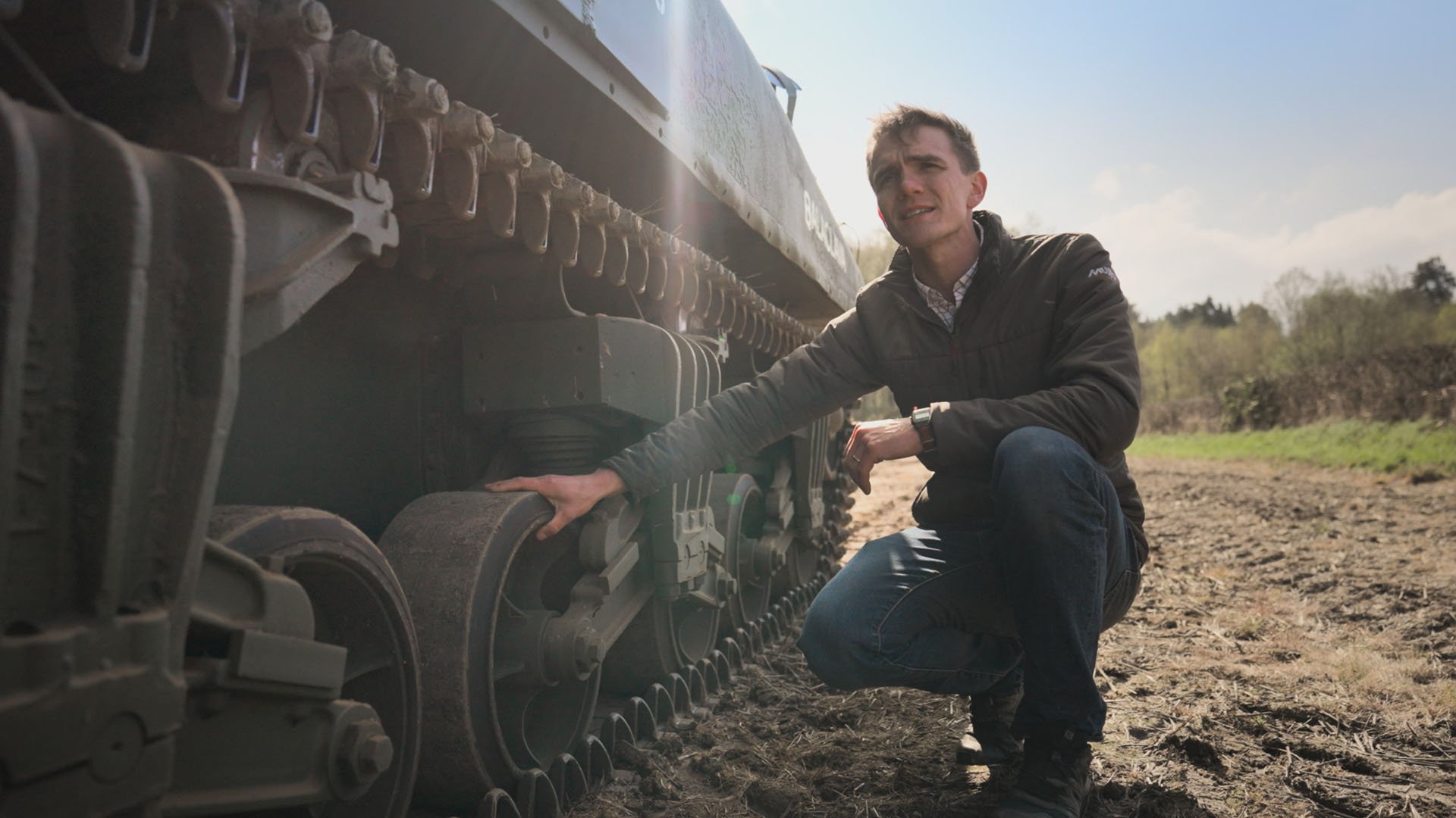 Matt Winters kneels next to a Sherman tank.  This is from WWII: Secrets From Above, season 2. [Photo of the day - September 2023]