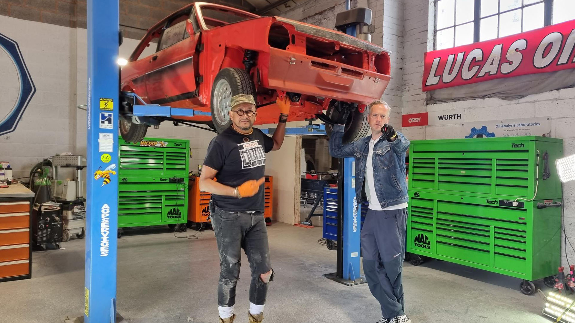 At the workshop, Fuzz Townshend and Tim Shaw stand by the suspended XR2. Townshend is pointing... [Photo of the day - April 2024]