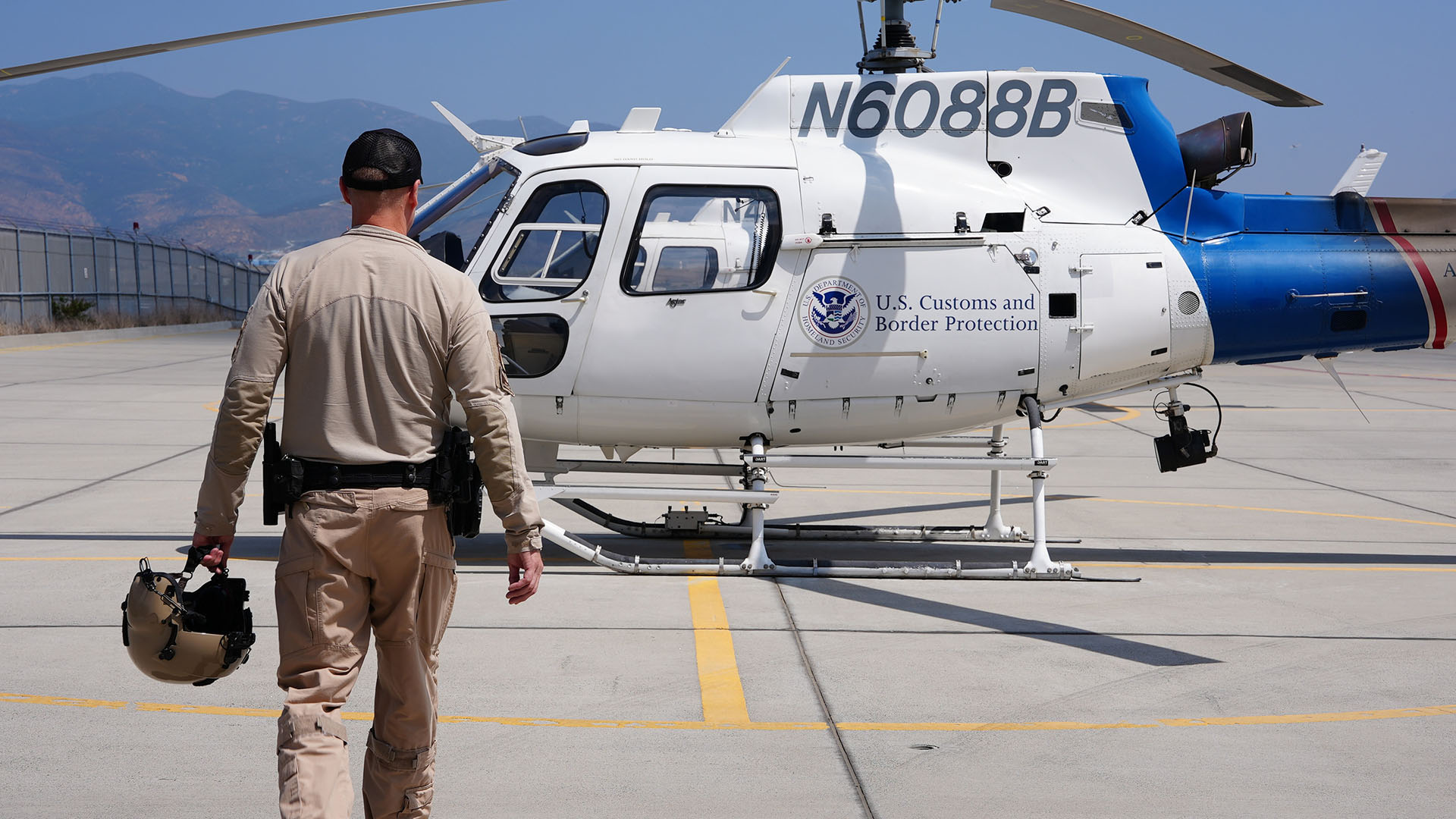 Air Enforcement Agent Murray is holding his helmet as he walks across a tarmac to a CBP air... [Photo of the day - May 2024]