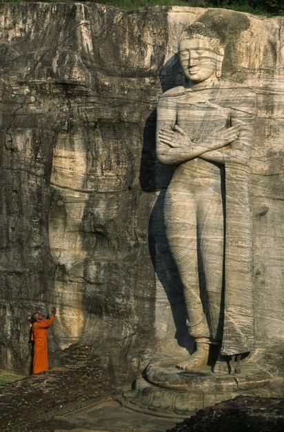 Buddhist monk at the foot of a tall stone Buddha sculpture on a hill. Sri Lanka. [Photo of the day - November 2011]