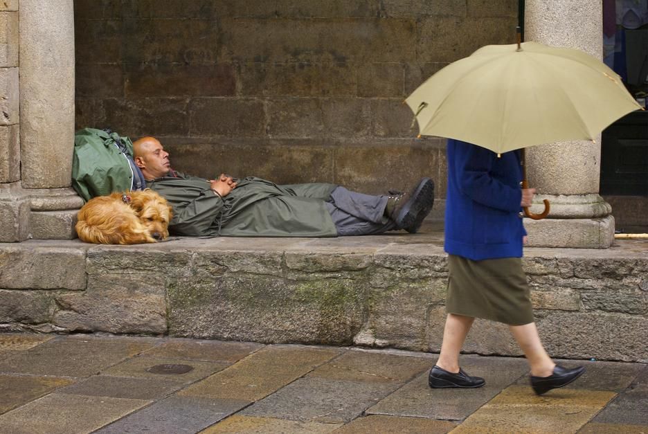 A woman carrying an umbrella passes a man on a pilgrimage sleeping in Santiago de Compostela,... [Photo of the day - April 2011]